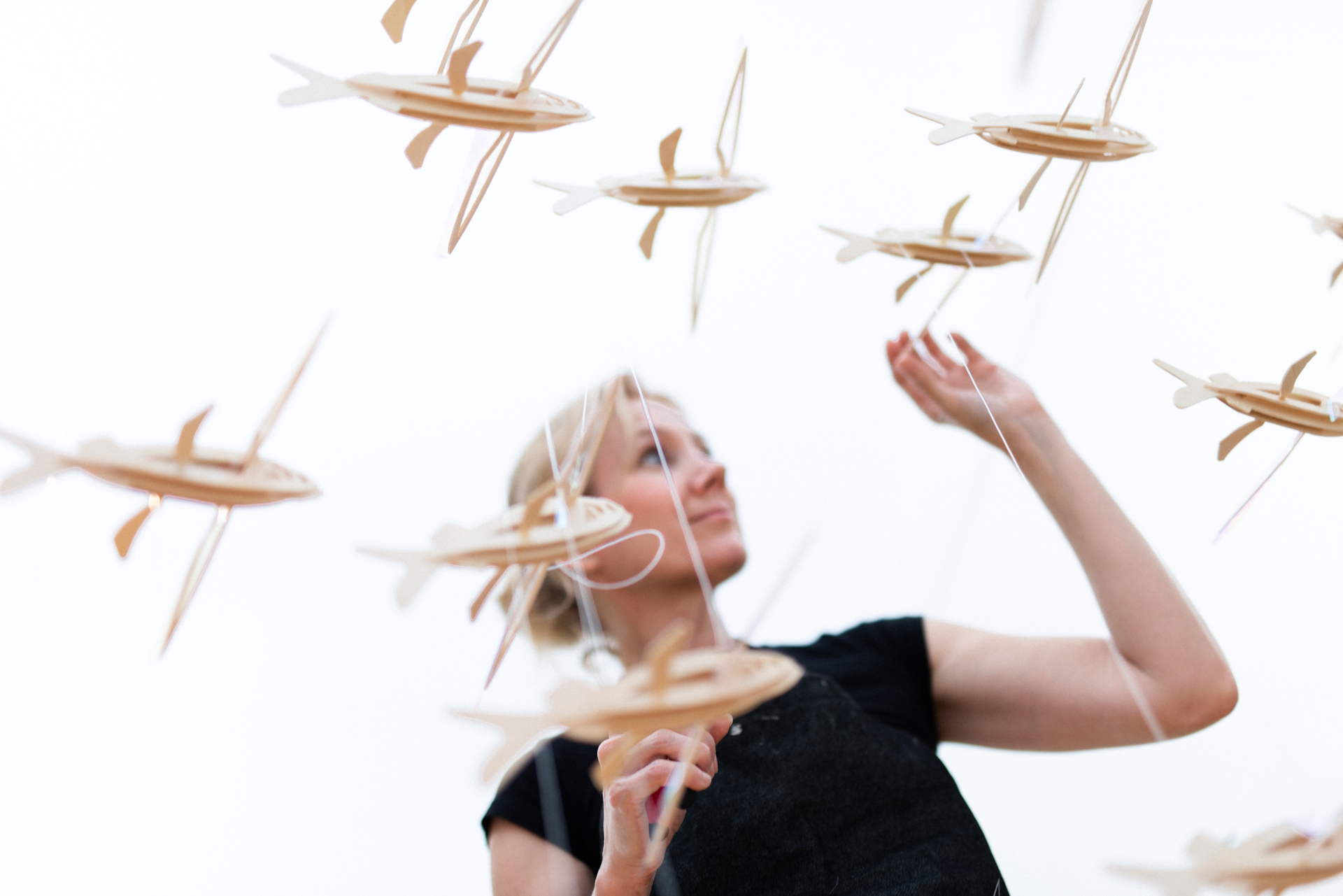 Sarah Hatton standing amid many wooden flying fish suspended by fishing line